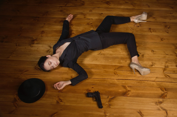 Woman in a black suit with gun lying on the floor - Foto, afbeelding
