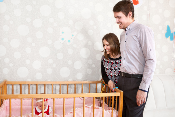 Happy Caucasian parents standing near baby bed and looking at their child - Foto, Bild