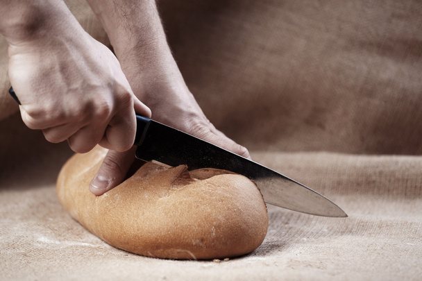 Αρσενικό χέρια ψωμί κόβεται με μαχαίρι - Φωτογραφία, εικόνα