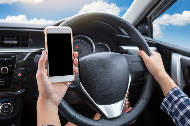 Fiatal nő vezető használ érintőképernyős okostelefon és kézi kormány egy autó kék ég és felhő háttér - Fotó, kép