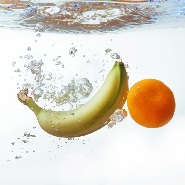 bananen en oranje viel in het water, geïsoleerd op wit - Foto, afbeelding