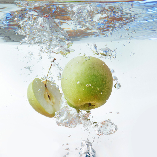 Green apple under water with a trail of transparent bubbles. - 写真・画像