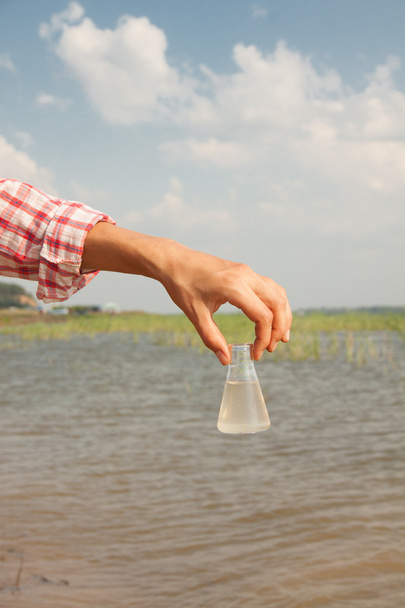 Prova di purezza dell'acqua. Pallone chimico a mano con liquido, lago o fiume sullo sfondo
. - Foto, immagini
