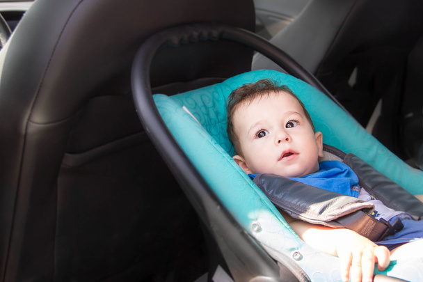 Portrait of toddler boy in car seat. Little smiling baby child fastened with a seat belt portrait of adorable happy baby boy sitting in the car seat. concept in safety in the car. - Photo, Image