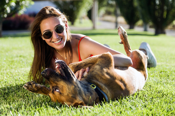 Beautiful young woman playing with her dog in the park. - Фото, изображение