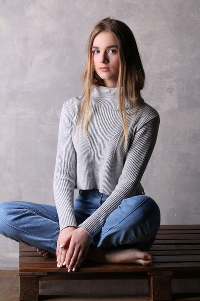 Girl in pullover sitting on a deck. Gray background - Φωτογραφία, εικόνα