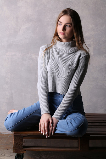 Model in sweater sitting on a deck. Gray background - Zdjęcie, obraz