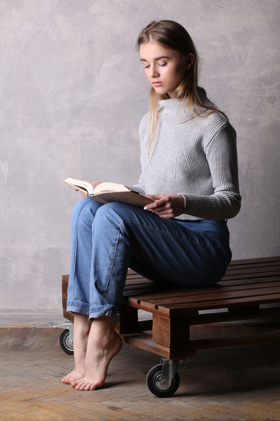 Teen in sweater reading a book. Gray background - 写真・画像