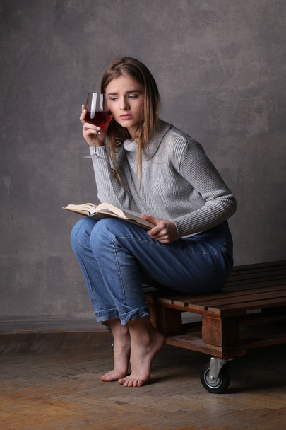 Girl holding book and glass of wine. Gray background - Photo, Image