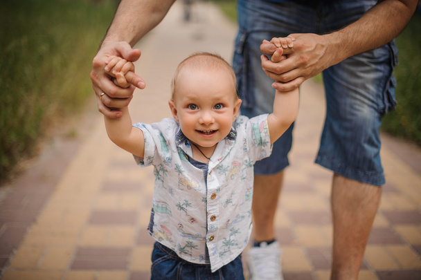 Baby boy learning to walk and making his first steps holding hands of  father. - Foto, Imagem