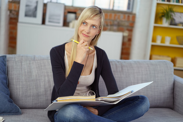 Thinking young woman sitting on sofa with notebook - Foto, Imagen