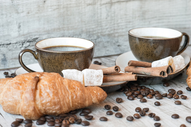 Cup of coffee with grains, croissant, turkish delight and cinnamon sticks on wooden background - Photo, Image