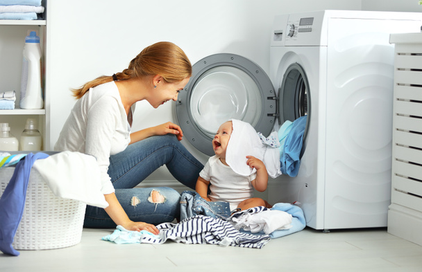 Mutter Hausfrau mit Baby faltet Kleidung in die Waschmaschine - Foto, Bild