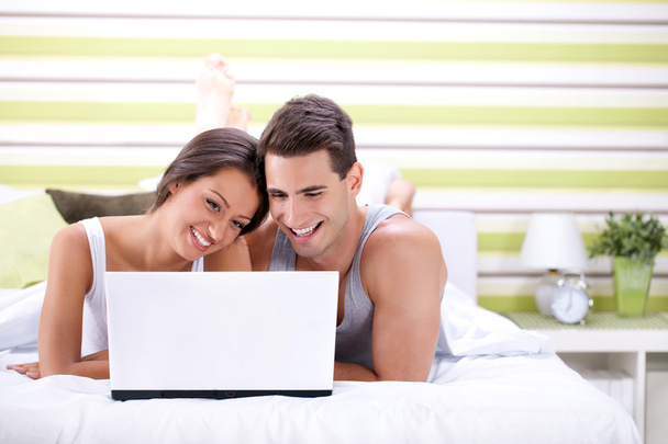 Young couple using laptop while lying on bed - Foto, imagen