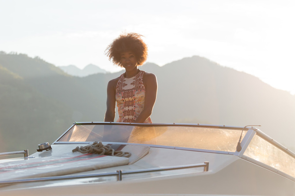 Summer vacation - young afro woman driving a motor boat on sunse - 写真・画像