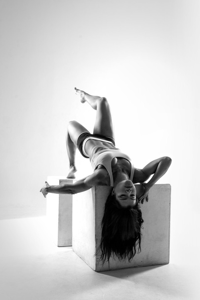 Muscular female body. Young strong athlete posing on cube. Black-and-white contrast photo - Zdjęcie, obraz