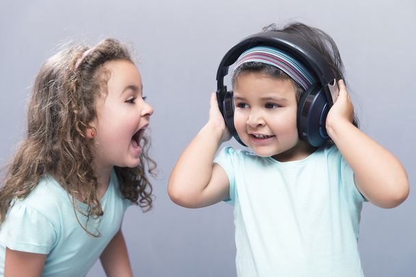 Older sister screaming at her younger sister in headphones - Foto, afbeelding