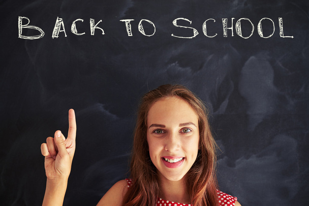 Portrait of beautiful schoolgirl pointing up with forefinger at  - Photo, Image