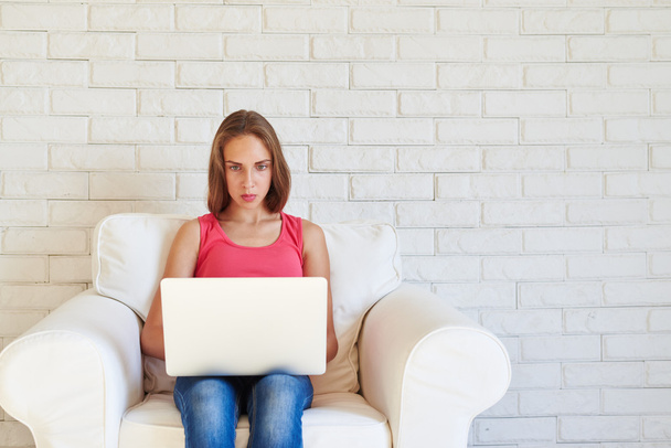 Tiener meisje in fauteuil werken op laptop met geconcentreerde exp - Foto, afbeelding