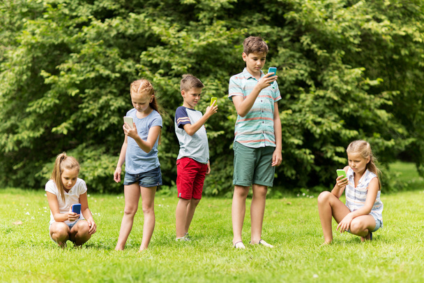 kids with smartphones playing game in summer park - Fotó, kép