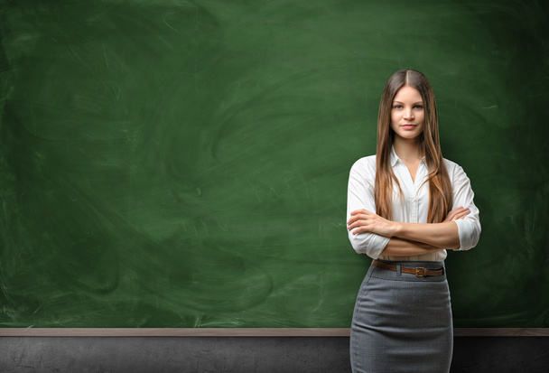 Young businesswoman with glasses standing in front of blank chalkboard - Φωτογραφία, εικόνα
