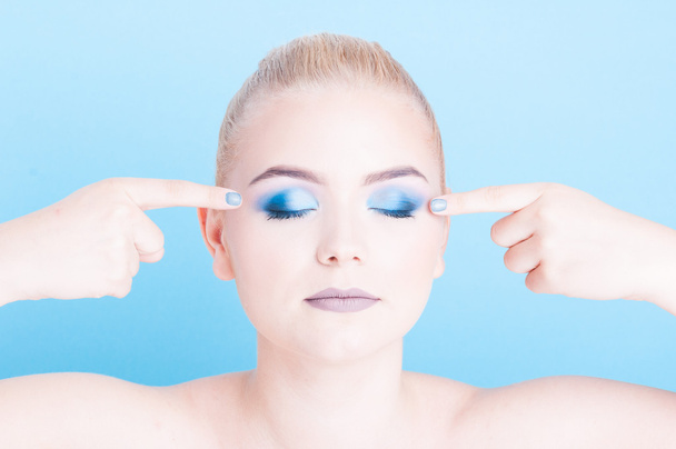 Portret van meisje wijzen op blauwe oogschaduw make-up - Foto, afbeelding