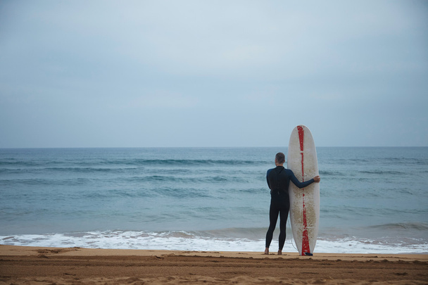 alter Surfer mit Surfbrett bleibt allein am Strand - Foto, Bild