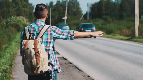Zadní straně mladík s batohem stopování na silnici v letní slunečný den. Palcem - Záběry, video