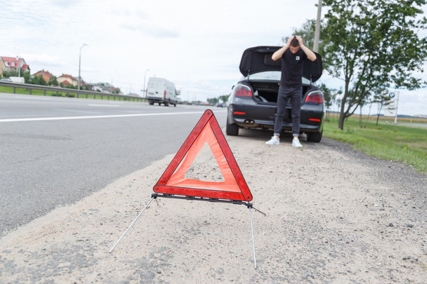 coche con una avería junto a la carretera, el hombre establece el triángulo de advertencia
 - Foto, imagen