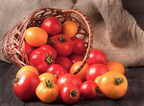 czerwone i żółte pomidory w wiklinowym koszu na drewnianym stole - Zdjęcie, obraz