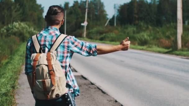 Zadní strana mladík s batohem stopování na silnici v létě slunečný den. - Záběry, video