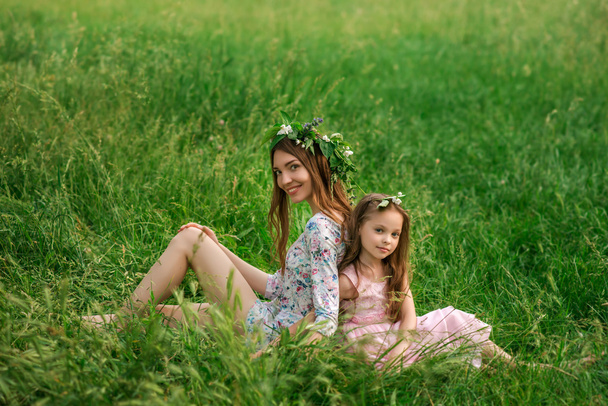 Lifestyle portret moeder en dochter zitten op gras in de  - Foto, afbeelding
