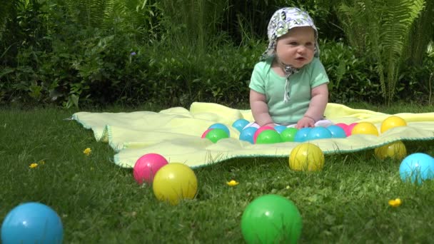 gezonde baby tijd tussen kleurrijke ballen op plaid in weide. 4k - Video