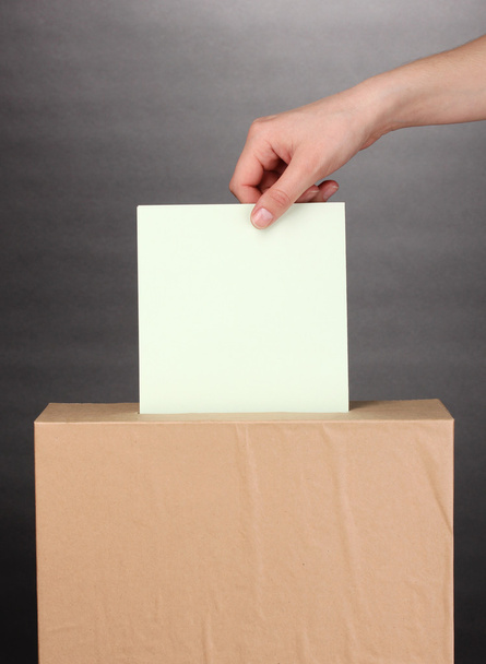 Hand with voting ballot and box on grey background - Foto, afbeelding