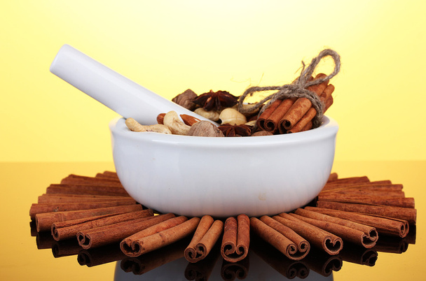 Composition of mortar with nuts and cinnamon on yellow background - Valokuva, kuva