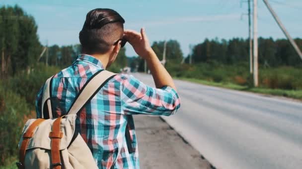 Face arrière du garçon avec sac à dos en lunettes de soleil auto-stop sur la route en journée d'été
. - Séquence, vidéo