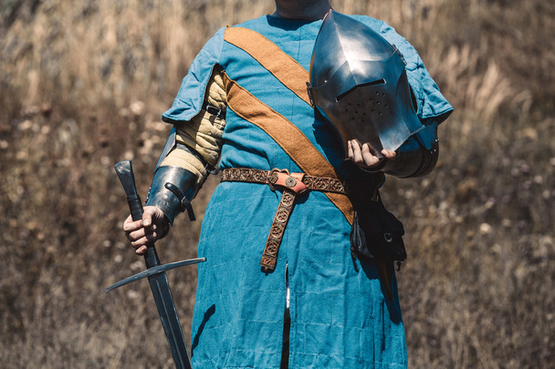 O cavaleiro de armadura de pé segurando uma espada e um capacete na mão
. - Foto, Imagem