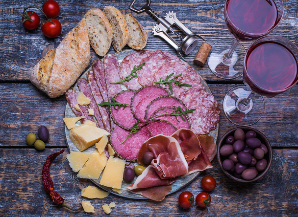 Red wine in a glass and a set of products - cheese, sausage, salami, olives, tomatoes, hot peppers, bread on a wooden board, background - Fotografie, Obrázek