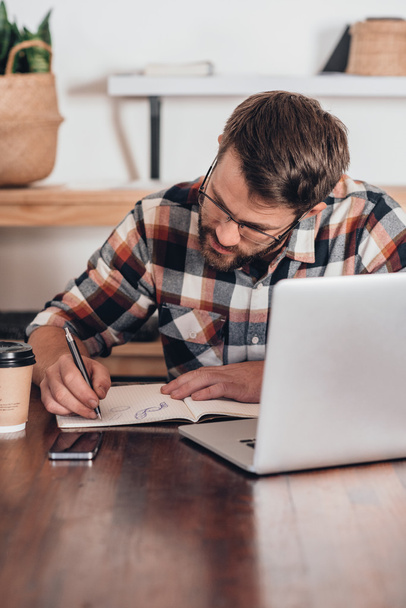 entrepreneur writing in notebook next to laptop - Φωτογραφία, εικόνα