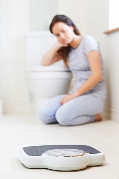 Unhappy Teenage Girl Sitting On Floor Looking At Bathroom Scales - Фото, зображення