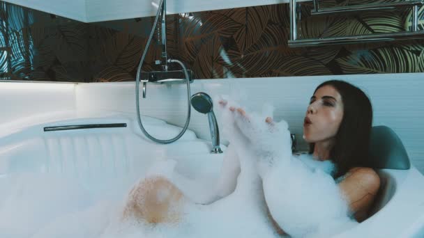 Chica feliz tomando baño lleno de espuma en el baño. Disfrutar. Soplar en espuma de jabón
. - Imágenes, Vídeo