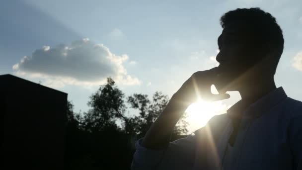 Μαύρος, μιλώντας στο τηλέφωνο, μπροστά από τον ήλιο κατά τη διάρκεια του ηλιοβασιλέματος, σιλουέτα - Πλάνα, βίντεο