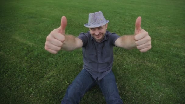 mladý muž módní klobouk sedí na trávě a pózování - Záběry, video