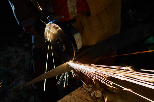 Robotnik obcinający metal szlifierką. Iskry podczas mielenia żelaza - Zdjęcie, obraz