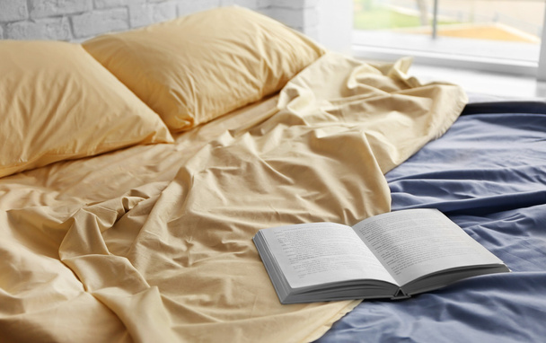 Opened book on crumpled bed in room - Fotoğraf, Görsel