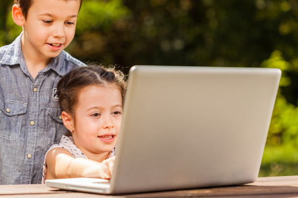 Enfants souriants dans le parc et à l'aide d'un ordinateur portable
 - Photo, image