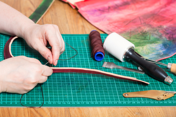 Ремесленник зашивает кожаный ремень для тисненой сумки
 - Фото, изображение