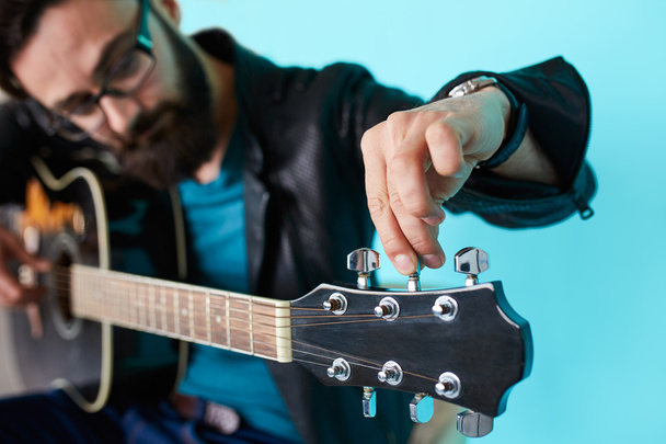 Parrakas hipsteri mies säätämässä kitaraa
 - Valokuva, kuva