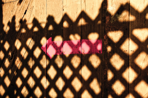 το ροζ βελάκι με σκιά του φράχτη σε ξύλινο πάτωμα - Φωτογραφία, εικόνα
