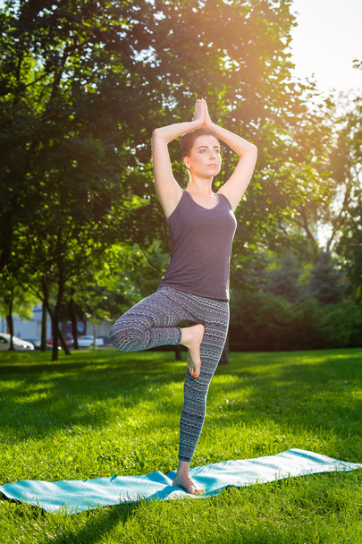 Young woman doing yoga exercises in the summer city park. - Zdjęcie, obraz